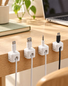 Four white cable organizers holding charging cables along a desk edge